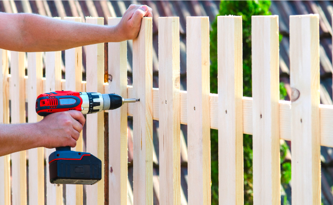 handyman repairing wooden fence with power tool