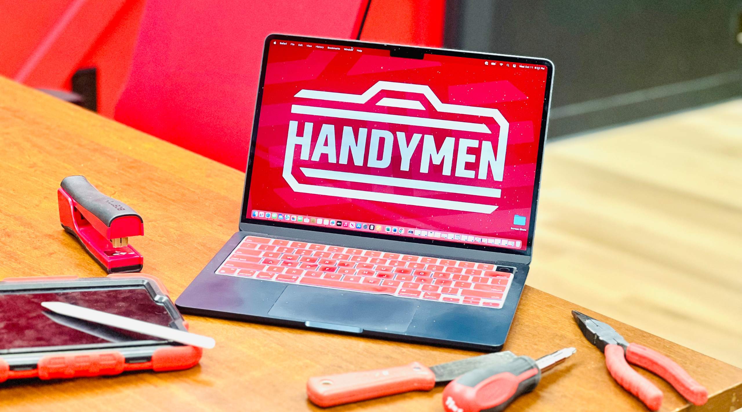Image of a laptop computer opened to the red "Handymen" logo. Computer is resting on a table with tools and a tablet.